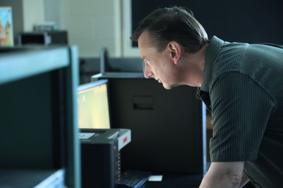 a view of a dark haired faculty member in a lab, leaning over a glowing computer screen 