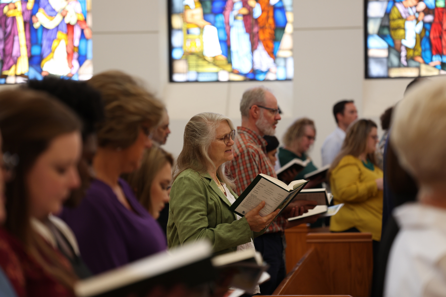 view of a group of faculty in a room with beautiful stained glass windows, reading and singing music together
