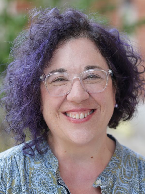 view of a smiling woman with purple hair and glasses and a blue shirt. She loves birds. 