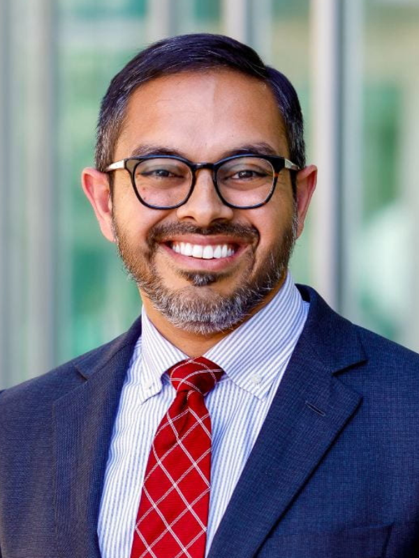 view of a smiling man wearing glasses, a blue suit, and a red tie