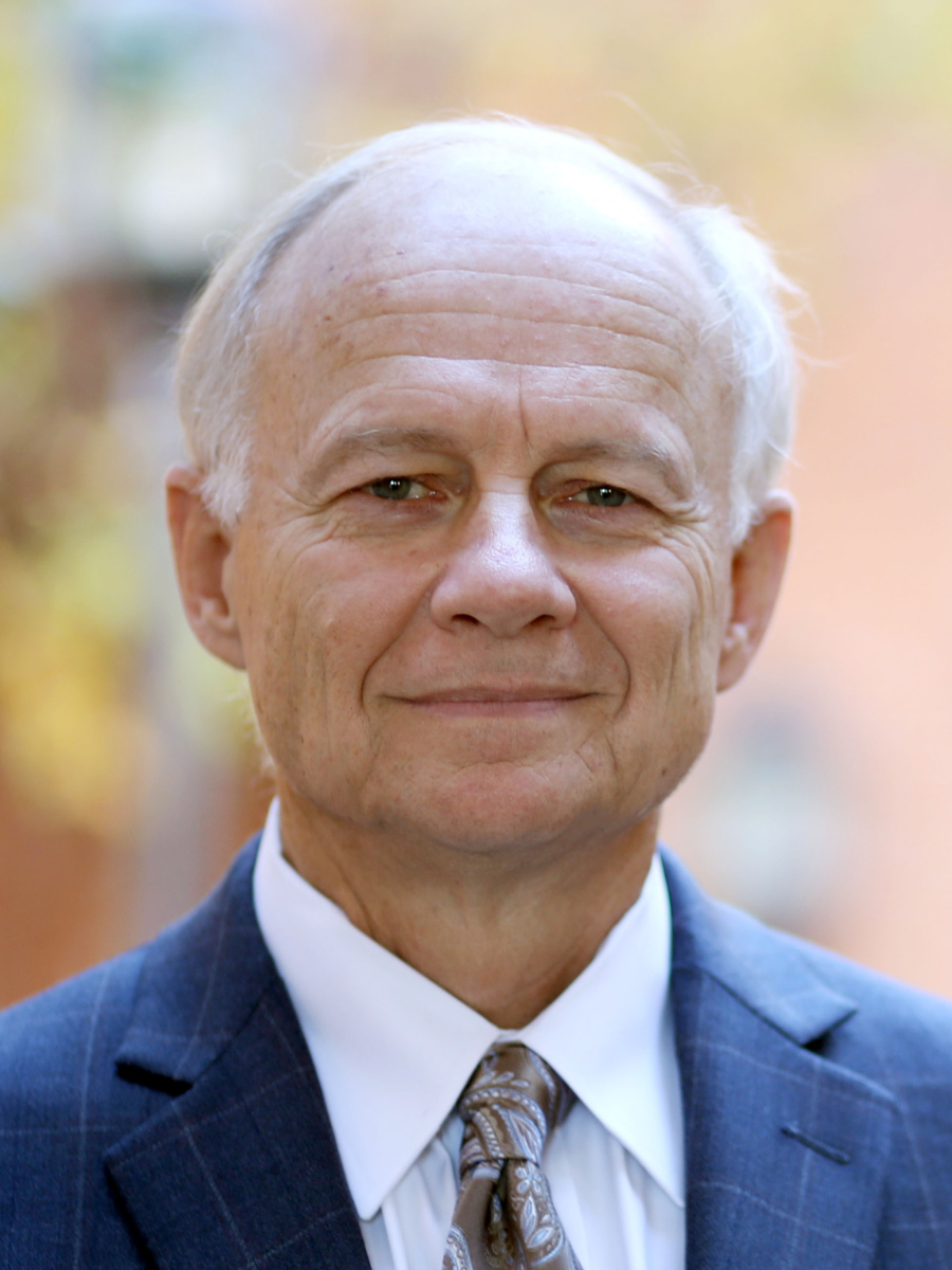 a view of a man facing the camera in a blue checkered suit with blue-grey eyes and white hair