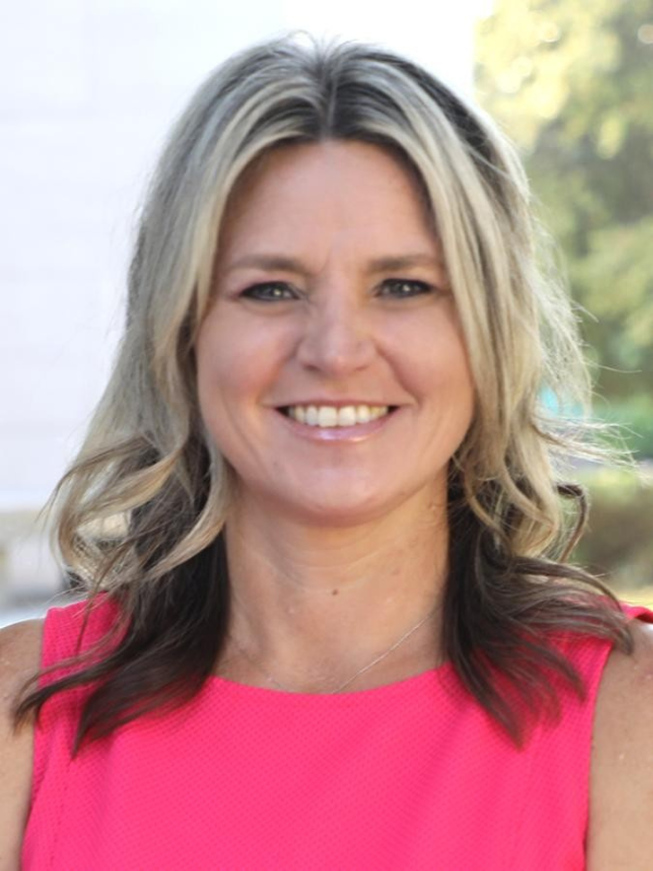 view of a smiling woman with a pink dress and highlighted hair looking at the camera